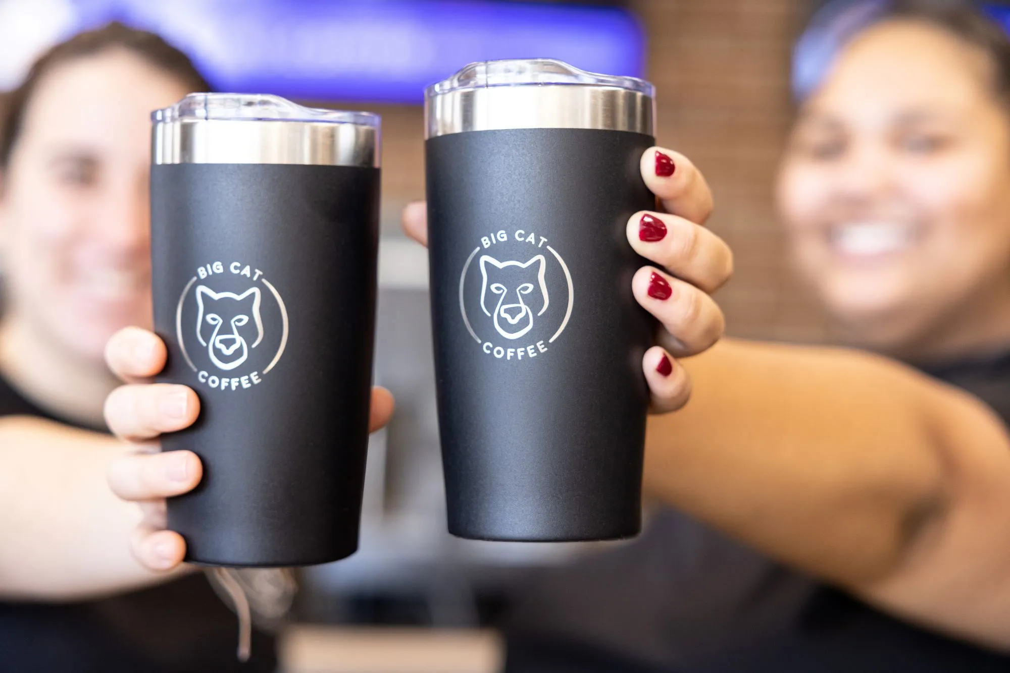 two student employees holding coffee cups that says "Big Cat Coffee"