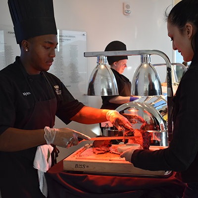 a cook serving meat from a buffet to a patron