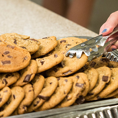 a woman's hand holding tongs selecting a chocolate chip cookie