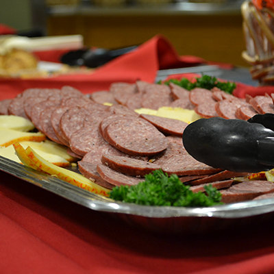 a close shot of a party tray with tongs, cheese, and meat sliced on it